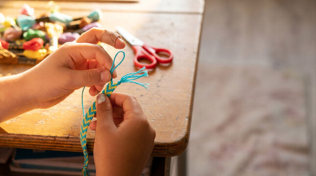 Two Young Hands Tying Cyan Friendship Bracelet Thread &ndash; Braided Friendship Macro &ndash; Elementary Social Bond &ndash; Afternoon Classroom Warm Light