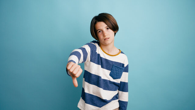 Boy expressing negative sentiment, showing dislike or rejection with a thumbs down gesture against a blue background