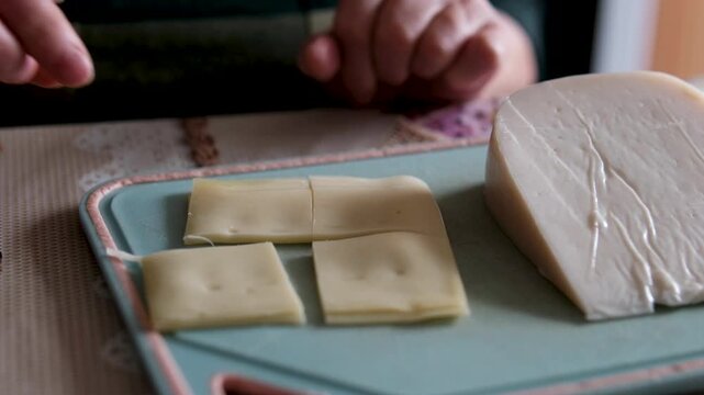 Pre-sliced packaged cheese is being arranged on plates, with sheep cheese placed on an old plastic board nearby. Close-up of a home kitchen scene highlighting dairy foods rich in calcium and simple.