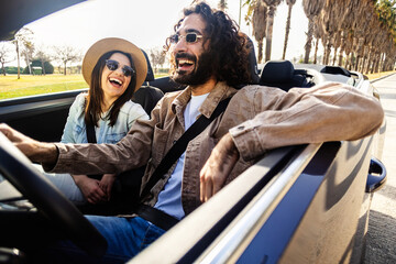 Obraz premium Young adult caucasian couple enjoying sunny convertible car ride. Relaxed man and woman traveling during summer vacation. Lifestyle and freedom concept.