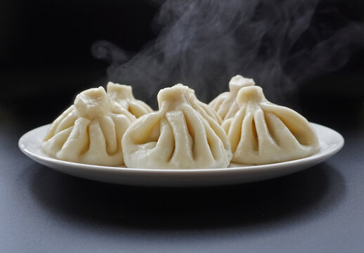 Several ready-made khinkali steamed.
Place four khinkali dumplings on a white platter, over which steam should rise.