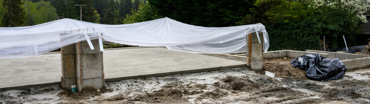 New residential house foundation construction, concrete slab poured and covered with plastic sheet for drying and curing
