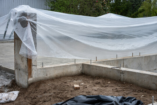 New residential house foundation construction, concrete slab poured and covered with plastic sheet for drying and curing
