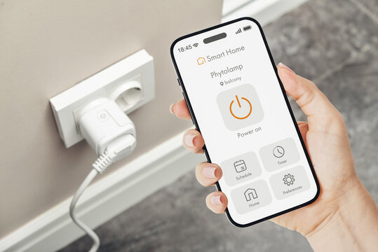 Female hand holding smartphone with smart home application interface for controlling a smart socket