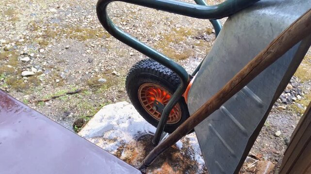 Close-up of a wheelbarrow wheel with an orange rim on a rainy day. Gardening work paused due to rain