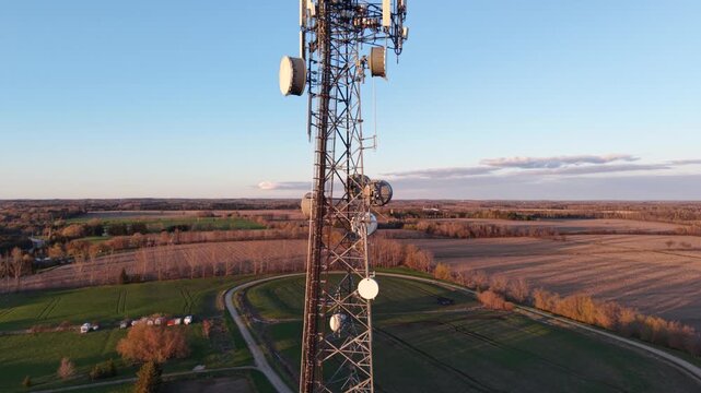 Vertical aerial drone ascent alongside a lattice telecommunications tower, showcasing microwave drum antennas and sector arrays against a rural landscape at golden hour