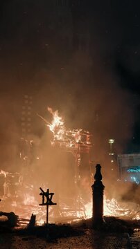 Wet muddy street surface covered in ash and debris reflects orange fire light after a falla burns down during Las Fallas La Crema in Valencia