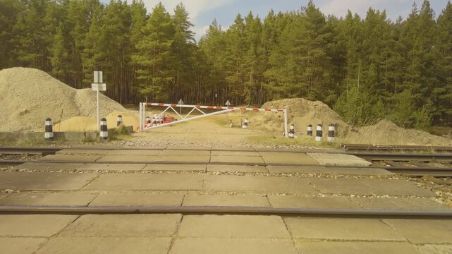 Construction site with railway crossing. Railway crossing amid gravel and forest setting. Scene showing railway tracks crossing gravel site with sand heaps and natural forest background