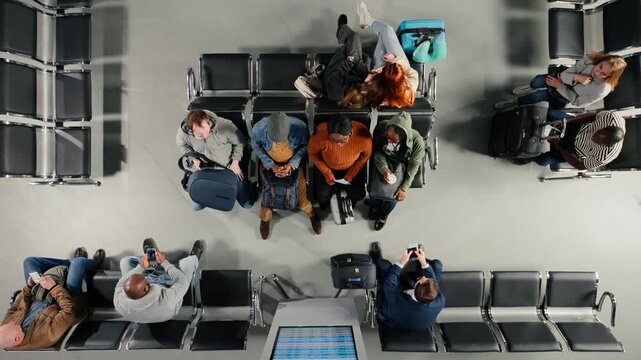 Top down view of troubled tourists in airport distressed by plane delays shown on departure board. Passengers upset by canceled flights announcement on FIDS display, high angle shot