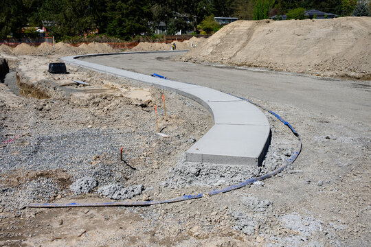 New housing development construction site at earthwork stage, road graded, concrete  sidewalk poured, temporary lay-flat hose for pumping out groundwater
