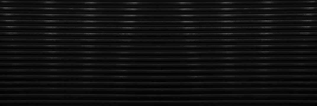 black corrugated metal wall background texture with vertical lines and rivets. Clean industrial surface for construction or architectural backdrop. Frontal view with bright natural light.