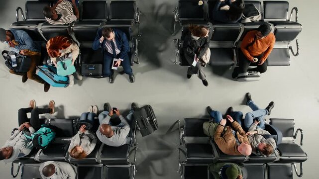 Top down view of people in busy airport terminal talking while waiting to catch plane. Diverse travelers with luggage and plane tickets chatting before boarding departure gate opens, high angle shot