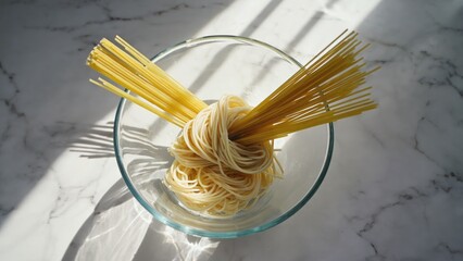 Raw pasta arranged in a glass bowl on a marbled surface with sunlight