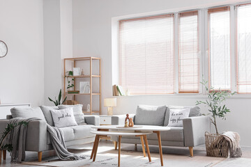 Fototapeta premium Interior of light living room with blinds on window, sofas and tables