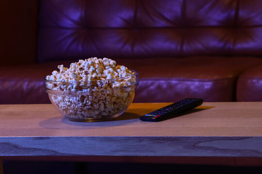 Tasty popcorn with TV remote controller on table in room at night