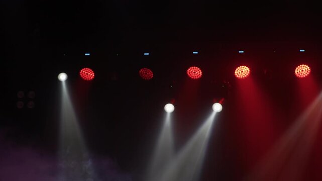 Clean frontal view of concert lighting rig with alternating white moving head and red LED par lights against dark ceiling, bright downward beam visible