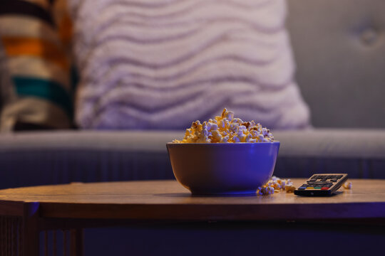 Tasty popcorn with TV remote controller on table in living room at night, closeup