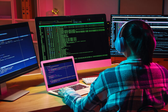 Female programmer with headphones working in office at night, back view