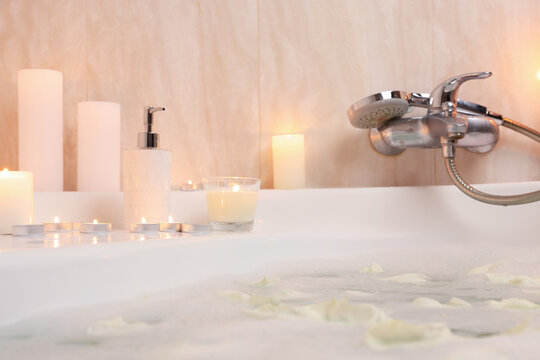 Romantic atmosphere. Bathtub with petals and burning candles in bathroom, closeup
