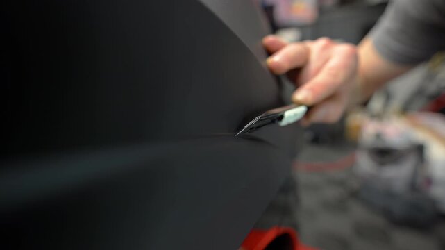 Close up of a applying matte vinyl wrap on a car body panel in a workshop. Automotive detailing process with protective film installation, smooth matte finish and precision work.