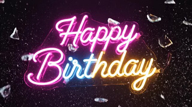 Illuminated neon script proclaiming celebratory 'Happy Birthday' glows vibrantly in pink and yellow hues against a textured, dark background surrounded by scattered crystalline fragments that