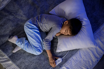 Cute little boy with pillow sleeping on electric heating pad in bedroom at night, top view © Pixel-Shot