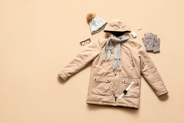 Stylish winter parka with smartwatch, earphones and accessories on beige background © Pixel-Shot