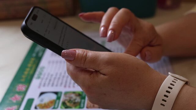 Woman using smartphone while choosing food from menu in restaurant closeup hands scrolling mobile app modern lifestyle cinematic video still