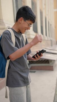 Happy male person looking at smartphone and gesturing with excitement after receiving good news in city. Vertical reels of real people, authentic emotions, success and positive reaction concept. 