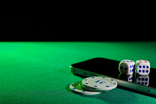Mobile phone with poker chips and dices on green table, closeup
