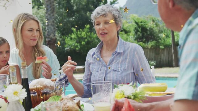 Mature woman starting speech, pointing, directing family at pool meal for food, gold stars drifting