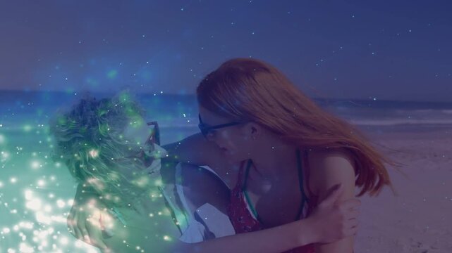 Two women turning hugging whispering on sand, laughing at camera while sparkle covering her for ads