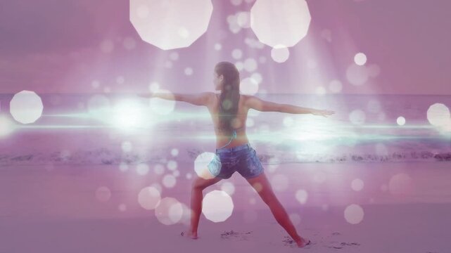 Woman shifting weight into right lunge doing fitness on sand with pink bokeh sweeping across body