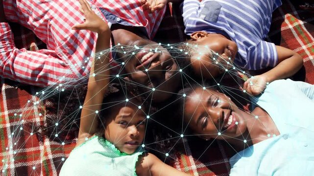 Family lying on red-white plaid blanket, cam starting and casting pulsing tech mesh over heads