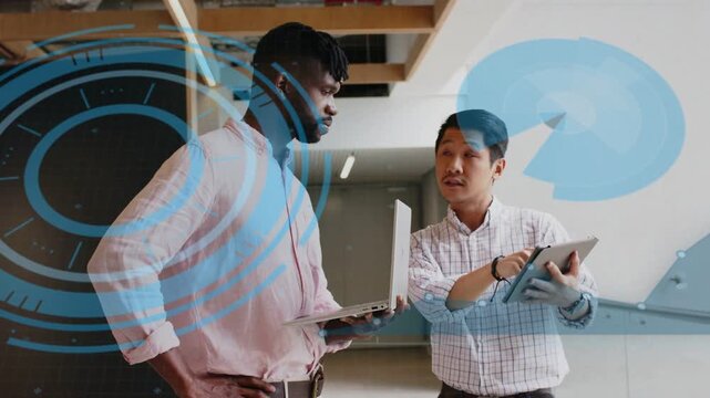 Two male colleagues tapping tablet, reviewing business data in corridor, HUD highlighting charts