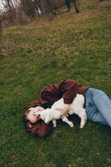 Naklejka premium Young woman lies on grass in casual jacket and jeans, cuddling a gentle goat kid, sharing a tender moment in nature, outdoor lifestyle scene with peaceful rural ambiance