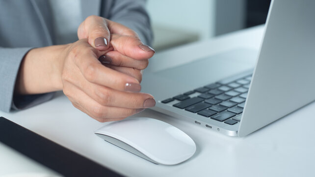 Trigger finger. Business woman painful thumb during working on laptop computer and mouse on table at office, occupational illness, office syndrome