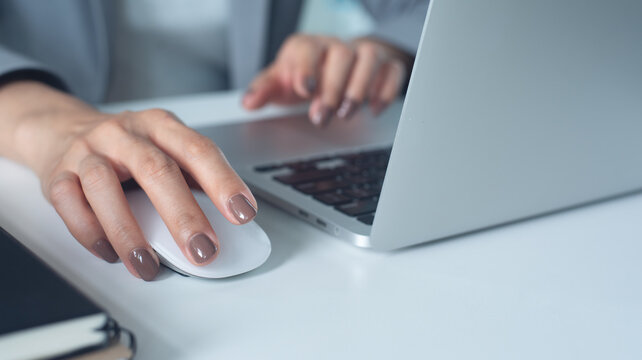 Business woman hand holding and clicking wireless computer mouse, working on laptop, surfing the internet, searching online information at office, close up