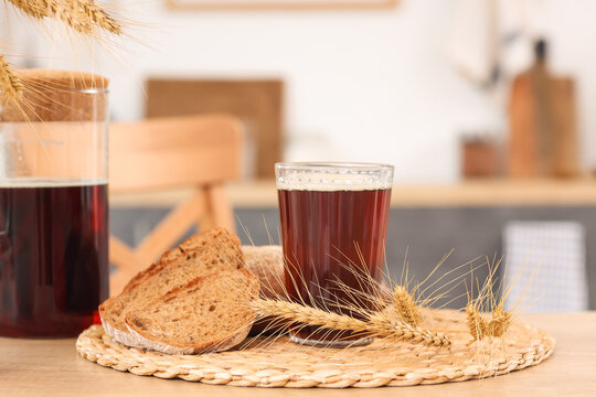 Jug of tasty kvass with glass, bread slices and spikelets on table in kitchen