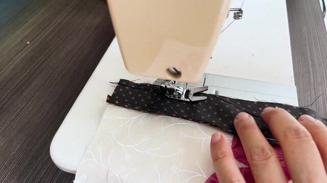 Close view of sewing machine stitching fabric strip as hand guides material under presser foot in tailoring workspace
