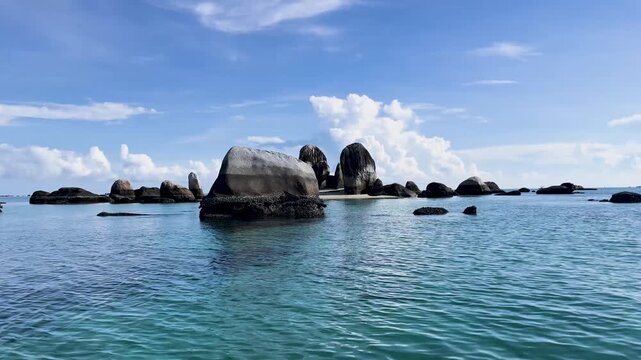 Boating in the clear turquoise sea calm water surrounding granite islet under bright sky in tropical setting