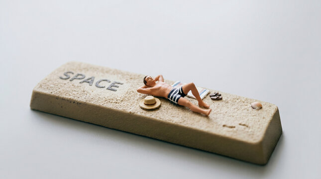 Miniature man sunbathing on a large keyboard spacebar representing leisure.