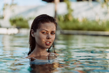 Fototapeta premium Woman in a pool with shoulders above water, facing the camera with a calm look, outdoors. Sunlit scene conveys leisure, wellness, and relaxed summer lifestyle.
