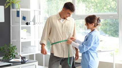 Fototapeta premium Female nutritionist measuring man's waist in clinic
