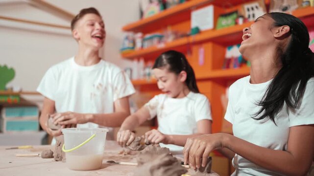 Happy diverse high school student modeling clay at pottery workshop. Cute children with mixed raced working and making cup of clay by using carving equipment at art lesson. Creative class. Edification
