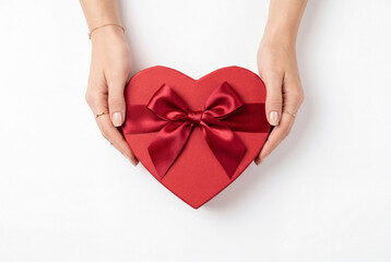 Obraz premium Hands holding a red heart shaped gift box with a silk ribbon on a white background