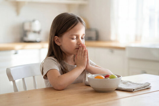 Young girl praying with hands together before eating a healthy meal. concept of faith and gratitude