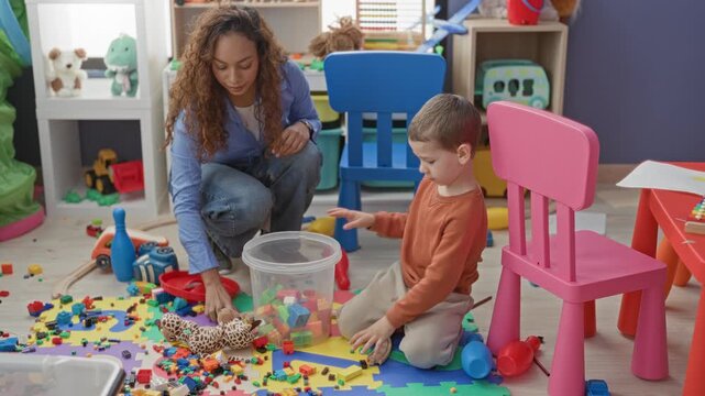 Woman kneeling, hand reaching for plastic blocks as young boy sorts toys on a playroom floor inside a building; learning calm.