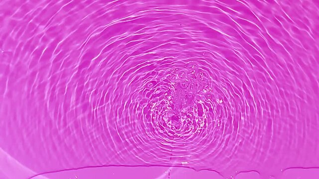 Pink water bubbles on the surface ripples. Defocus blurred transparent pink colored clear calm water surface texture with splash and bubbles. Water waves with shining pattern texture background