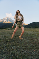 Fototapeta premium Relaxed woman in a grassy meadow explores an outdoor landscape, wearing casual attire. Bright natural light, expansive sky, and distant mountains convey freedom, nature, and lifestyle.